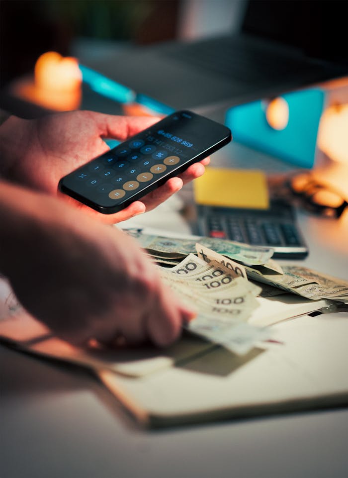 services-01 Hands using a smartphone calculator and handling cash on a desk, suggesting financial planning.