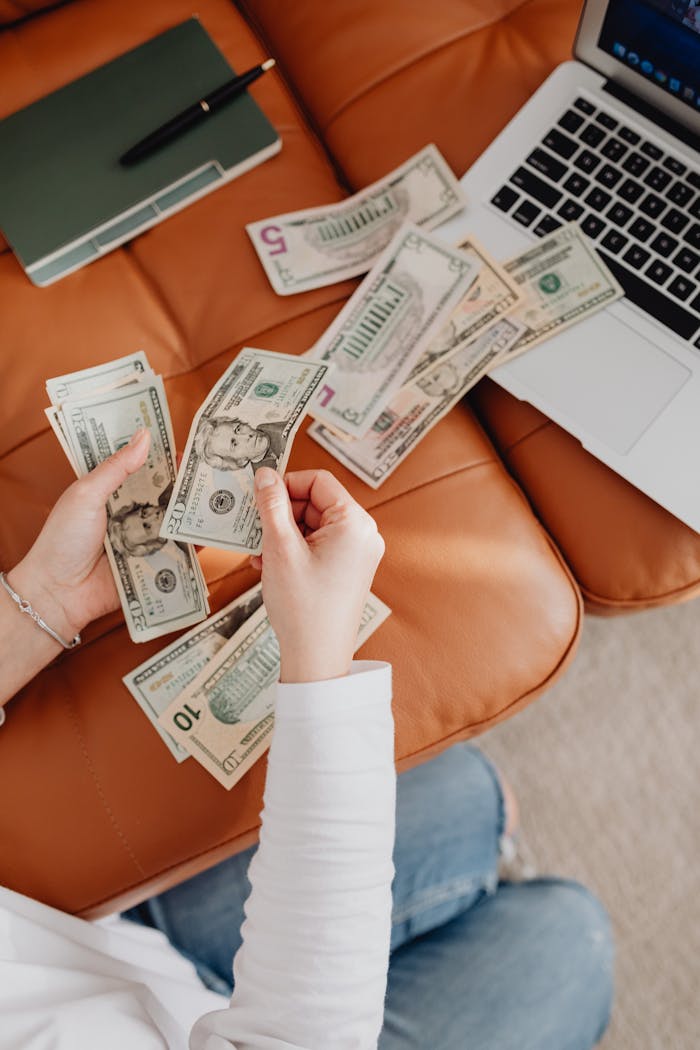 journey Person counting cash with a laptop and notepad on leather couch, representing finance and budgeting.
