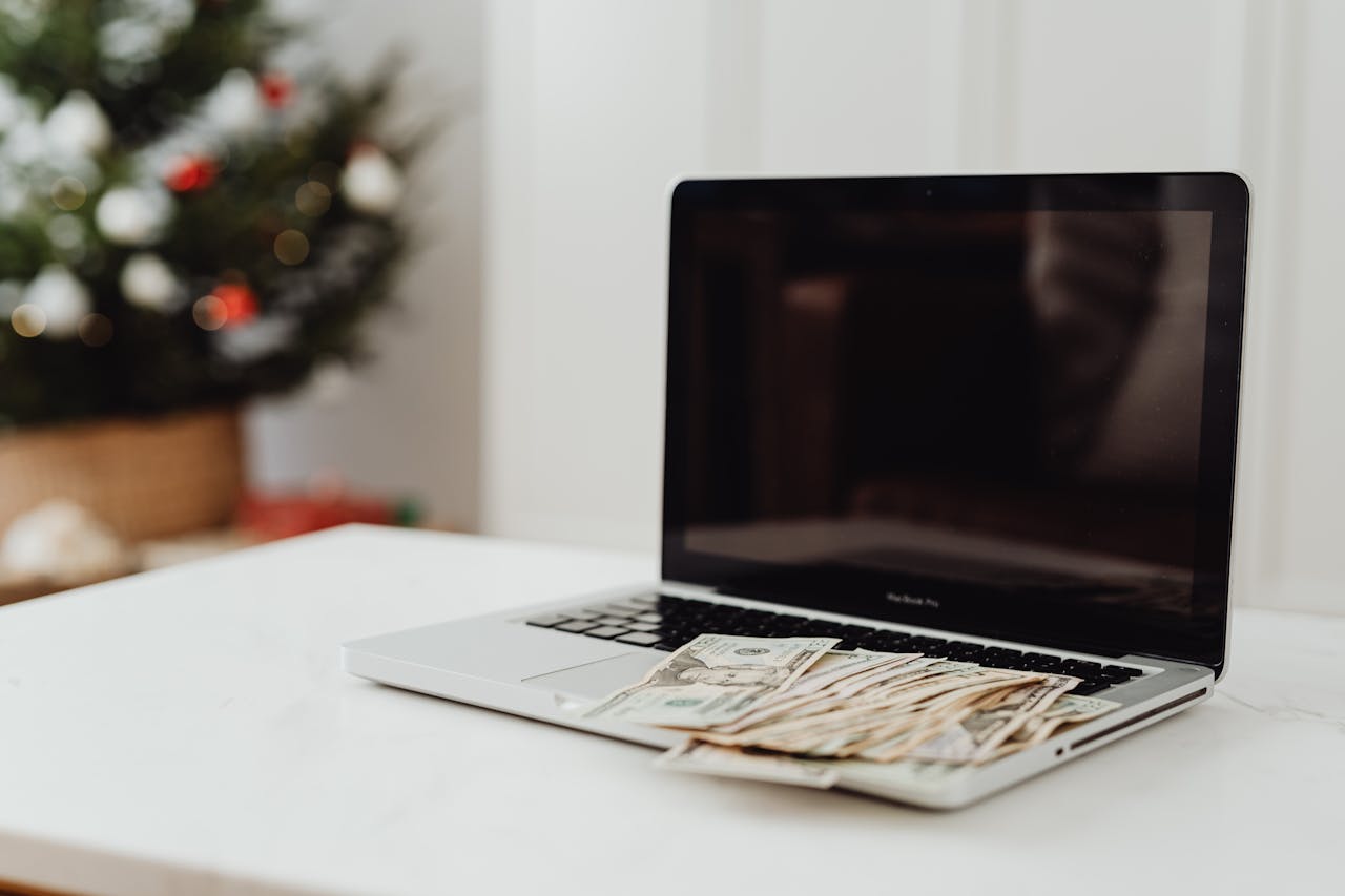 services-01 A laptop on a desk covered with cash, featuring a Christmas tree in the background.